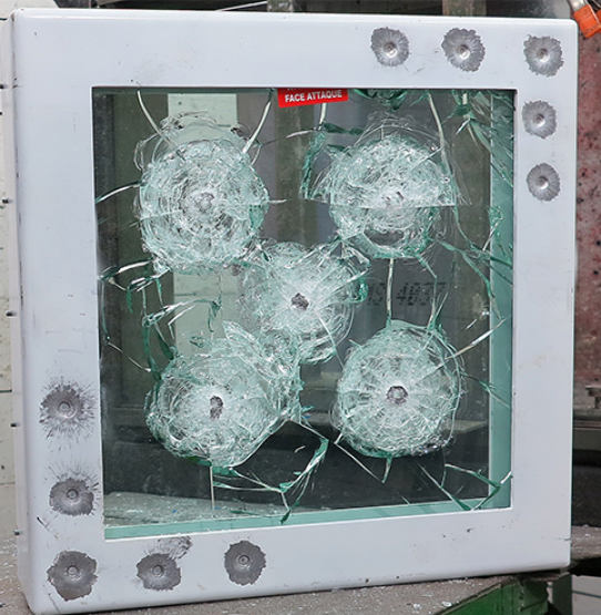A white frame surrounding a thick glass pane featuring several spider-web impact patterns and bullet holes on the edges.