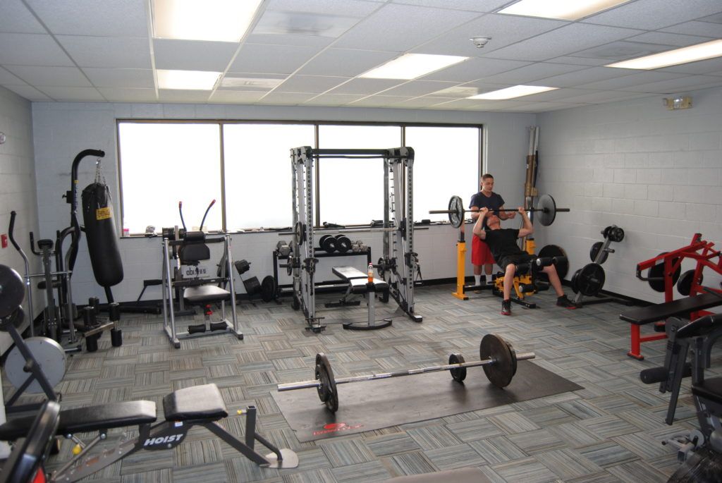 Gym interior with weightlifting equipment. A person is bench-pressing with assistance.