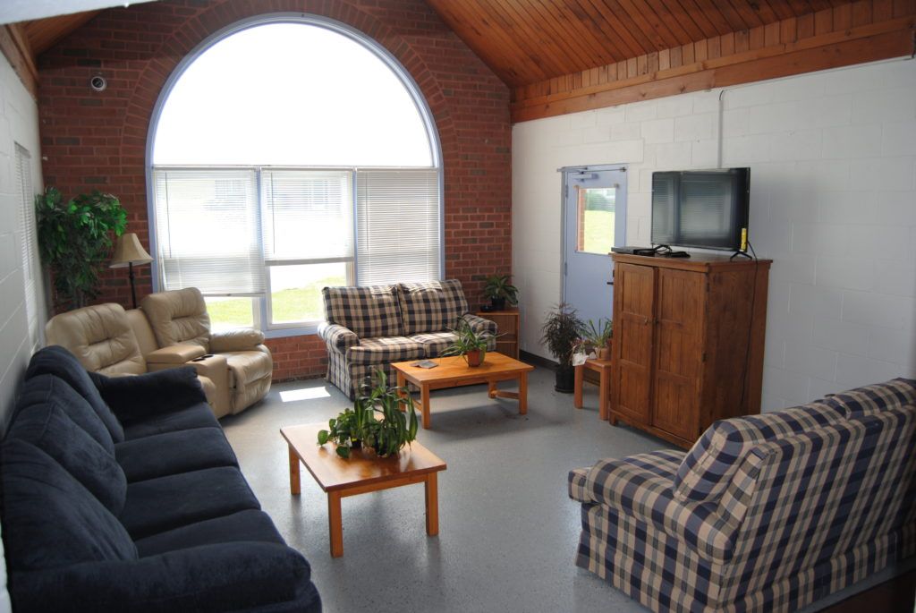 Interior of a brick-walled room with couches, tables, TV, and a large arched window with blinds.