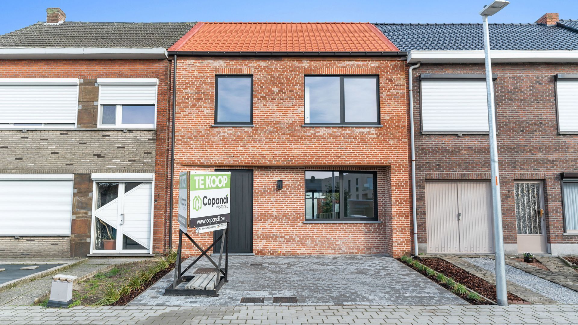 Een bakstenen huis met een te koop bord ervoor.