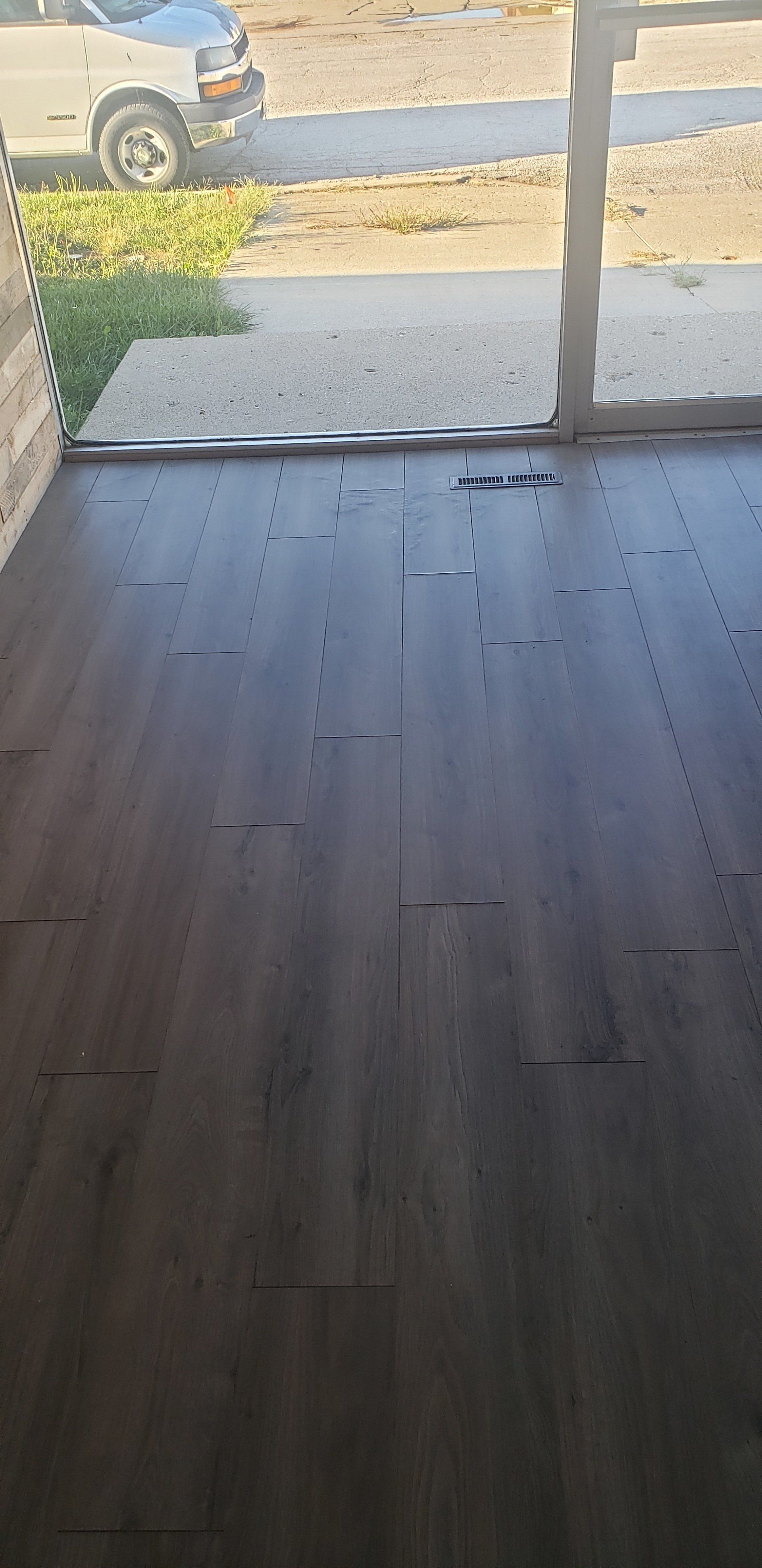 Dark gray wood flooring on a porch. The view is out to a street and car.