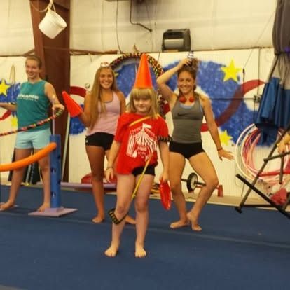 Group of people in a gymnasium; one with a cone hat, hula hoops, and juggling props.