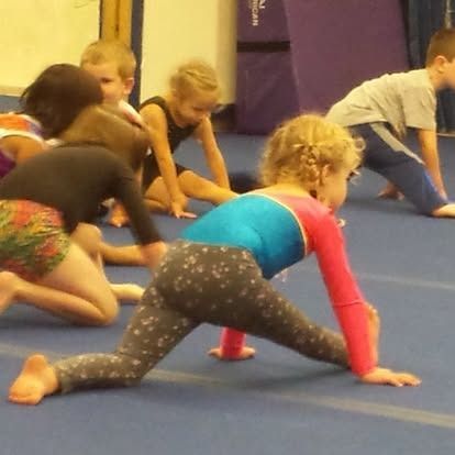 Young gymnasts stretching on blue mats in a gym. Girl in leggings doing the splits.