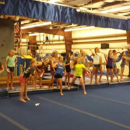 Girls throwing paper airplanes in a gym, a blue floor and equipment in the background.