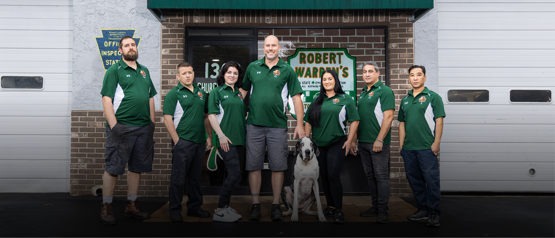 A group of people wearing green shirts stand in front of a building with a dog.