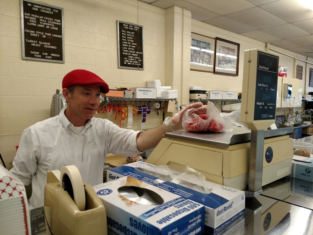 Shop worker in white uniform and red cap handing over a bag at a deli counter