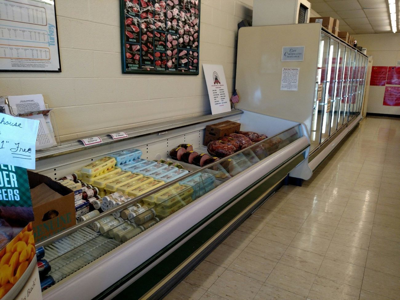 Grocery store aisle with long refrigerated display case holding assorted packaged foods and pastries.