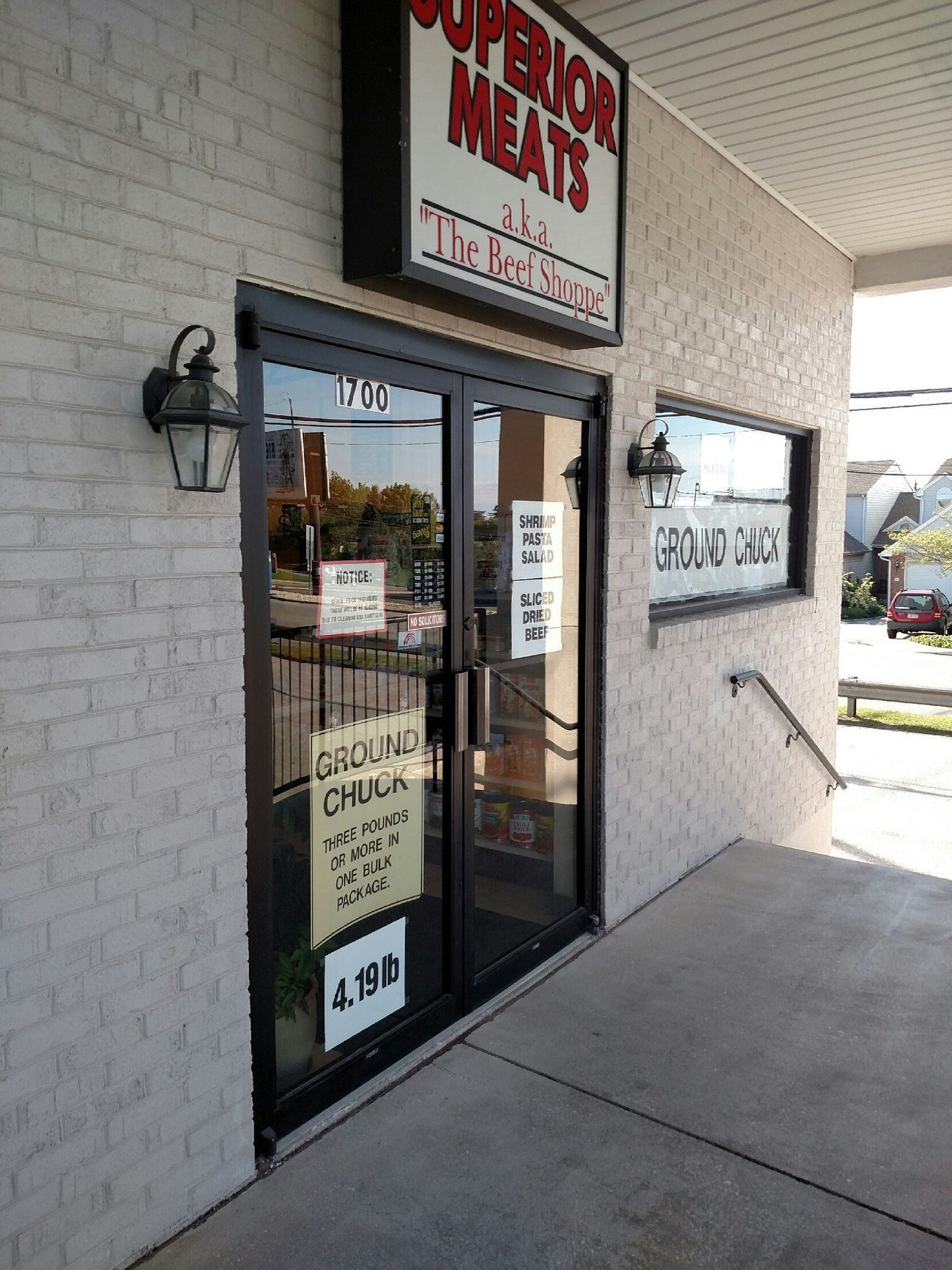Storefront entrance to Superior Meats with glass door, white brick exterior, and sidewalk ramp.