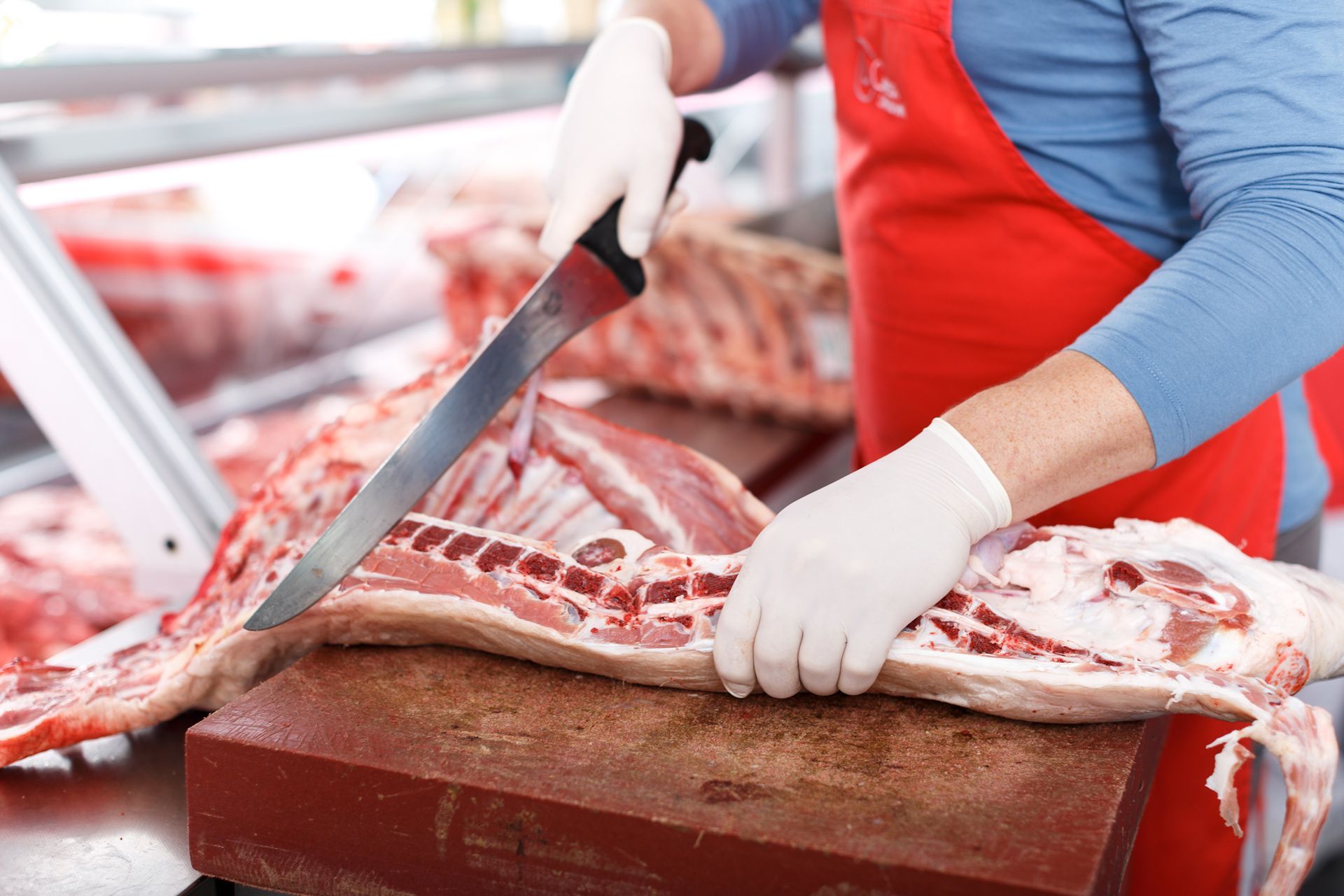 Butcher slicing raw meat on a wooden cutting board with a large knife