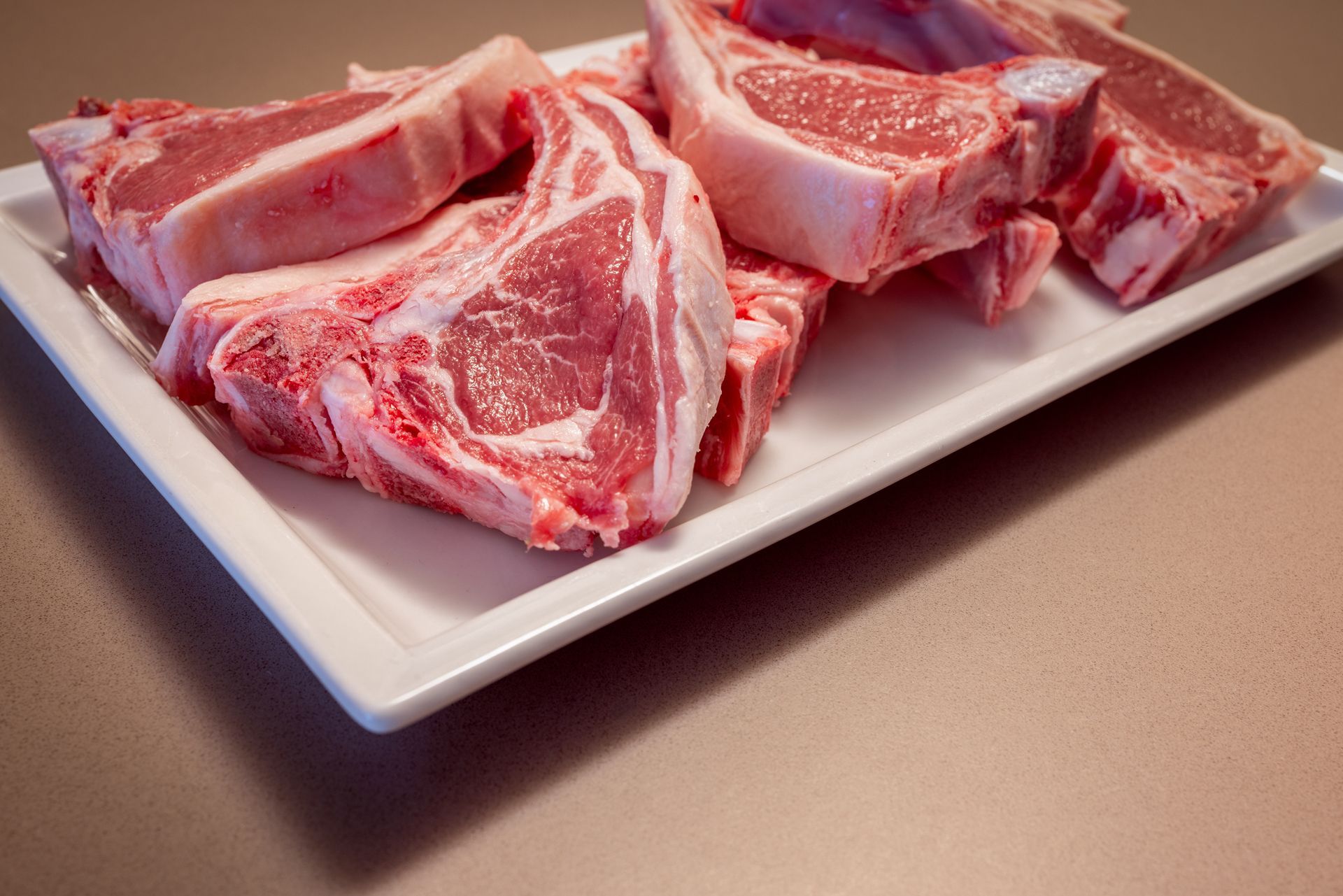 Raw lamb chops on a white rectangular plate, close-up view