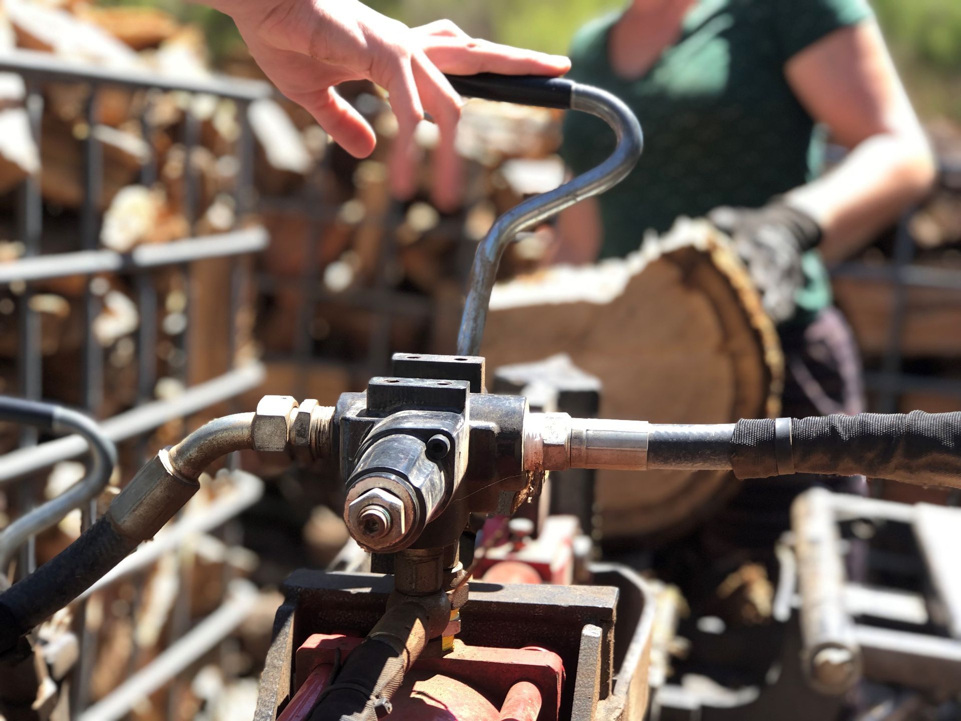 A person's hand operates the metal control lever of a hydraulic log splitter, with a large wood round nearby.