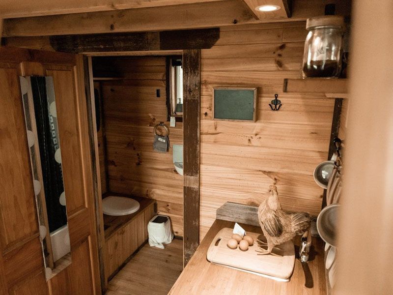 A rustic cabin interior featuring a wood-paneled bathroom with a toilet and a small kitchen counter with a ceramic rooster.