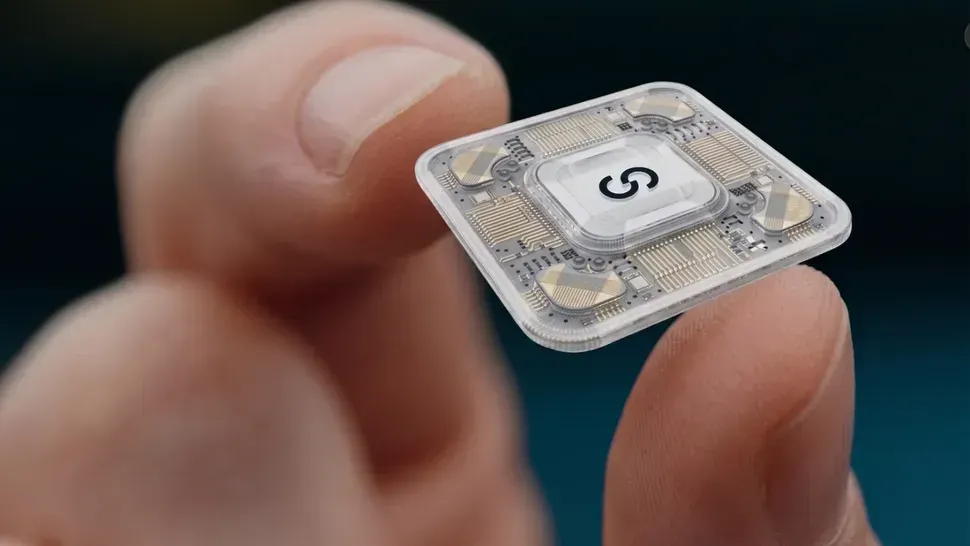 Close-up of a hand holding a tiny transparent electronic chip with a white center label.