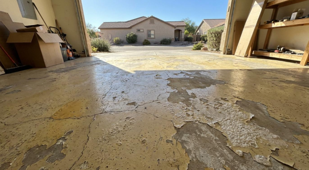Damaged concrete courtyard with peeling yellow coating, leading to a sunlit apartment building in the distance