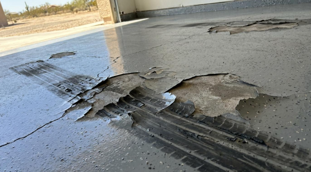 Damaged concrete floor with peeled-up layer and cracks near a garage or driveway area