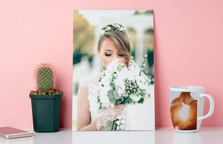 Une mariée tenant un bouquet blanc derrière un portrait encadré sur une étagère rose avec un cactus et une tasse