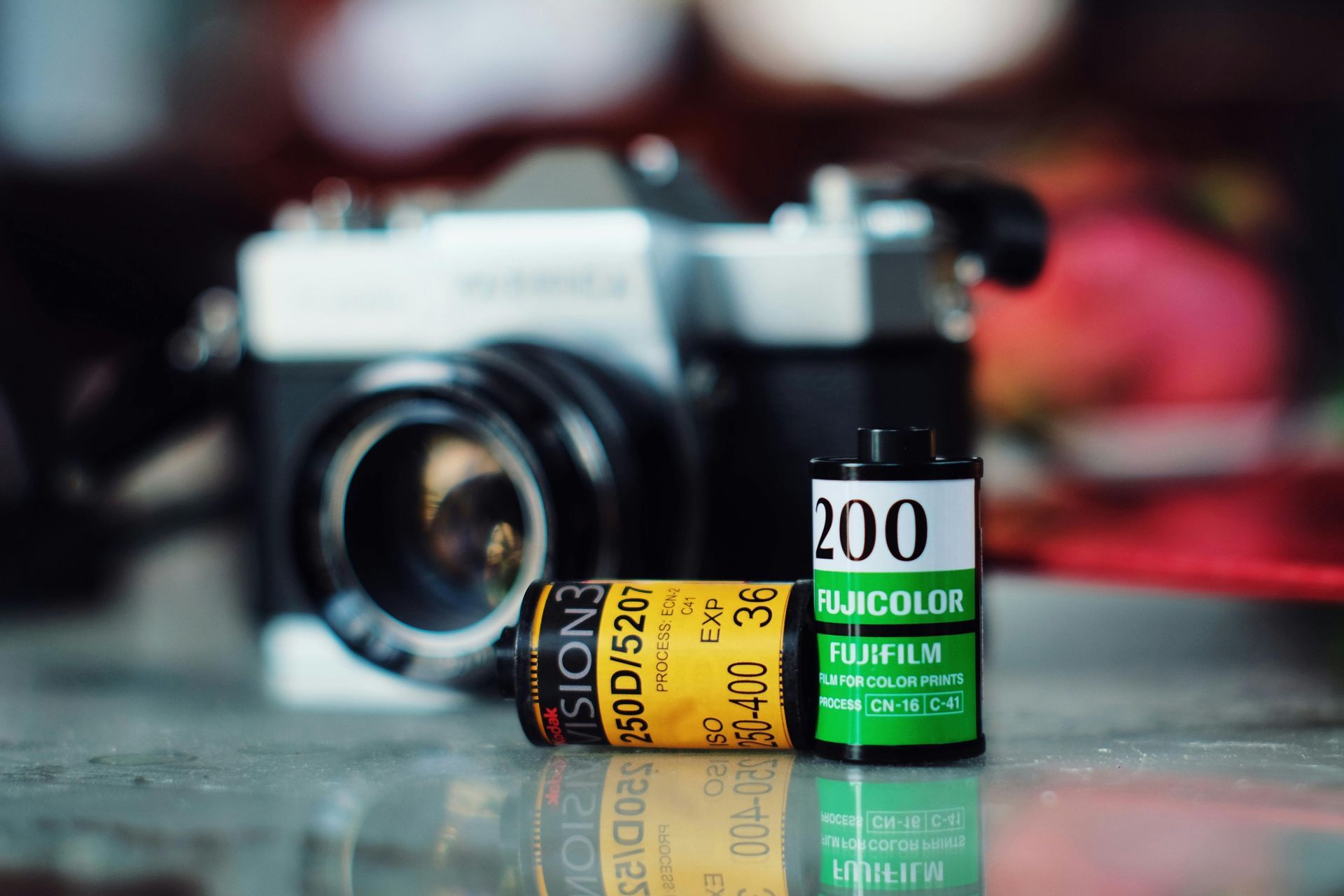 Des bobines de film sont posées à côté d'un appareil photo ancien sur une surface réfléchissante.