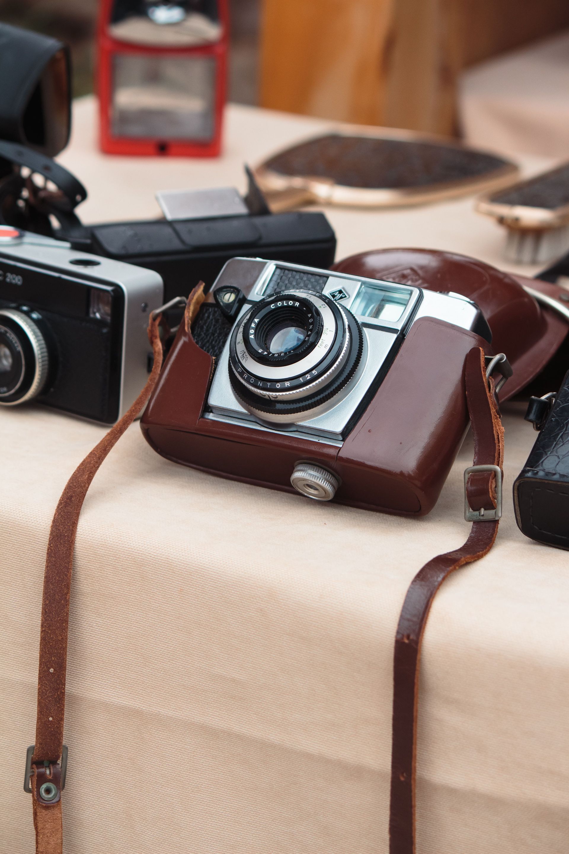Un appareil photo vintage posé sur une table dans un étui en cuir marron, avec d'autres appareils photo et accessoires à proximité.