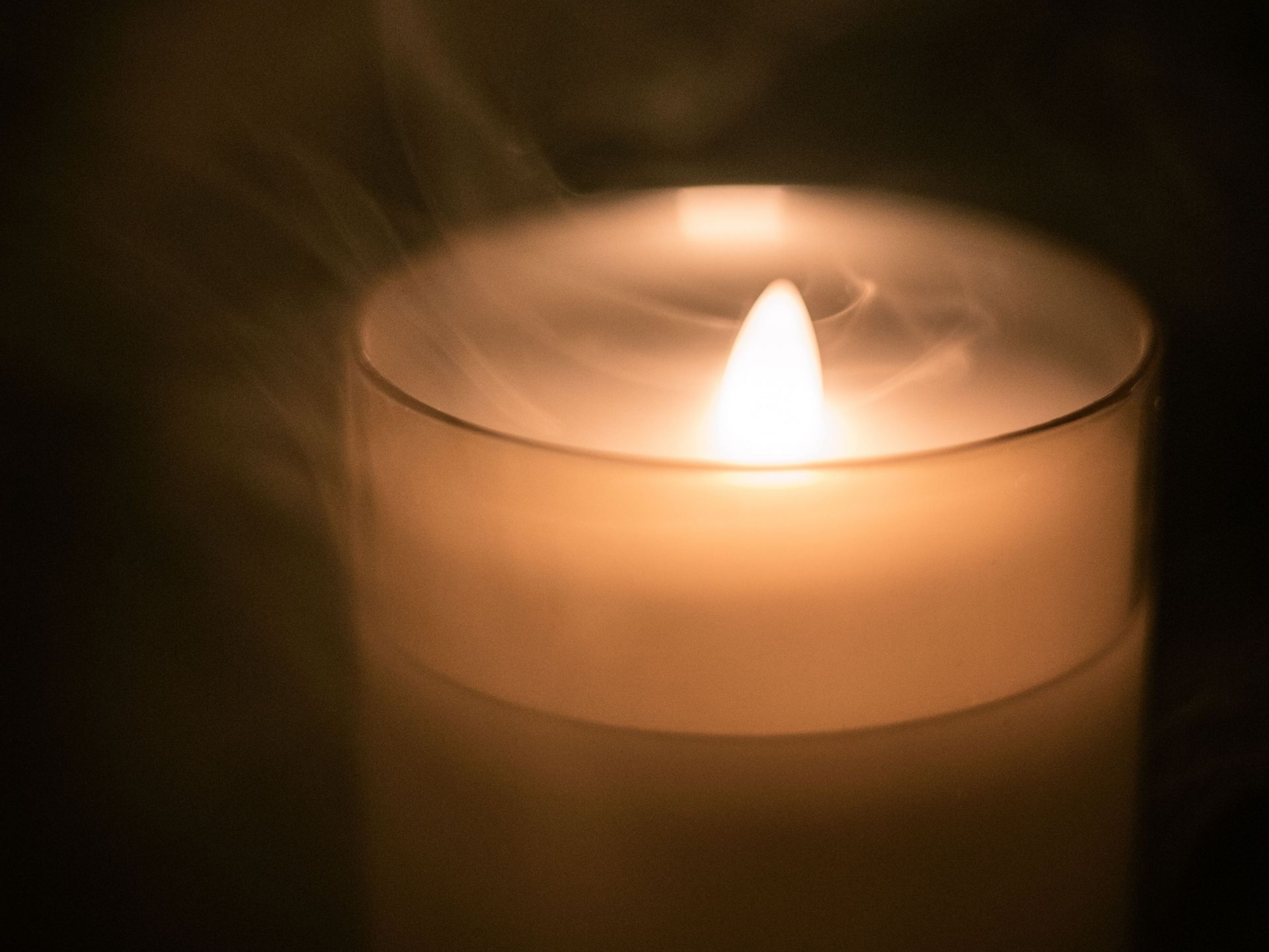 Lit candle in a glass holder, glowing warm orange against a dark background