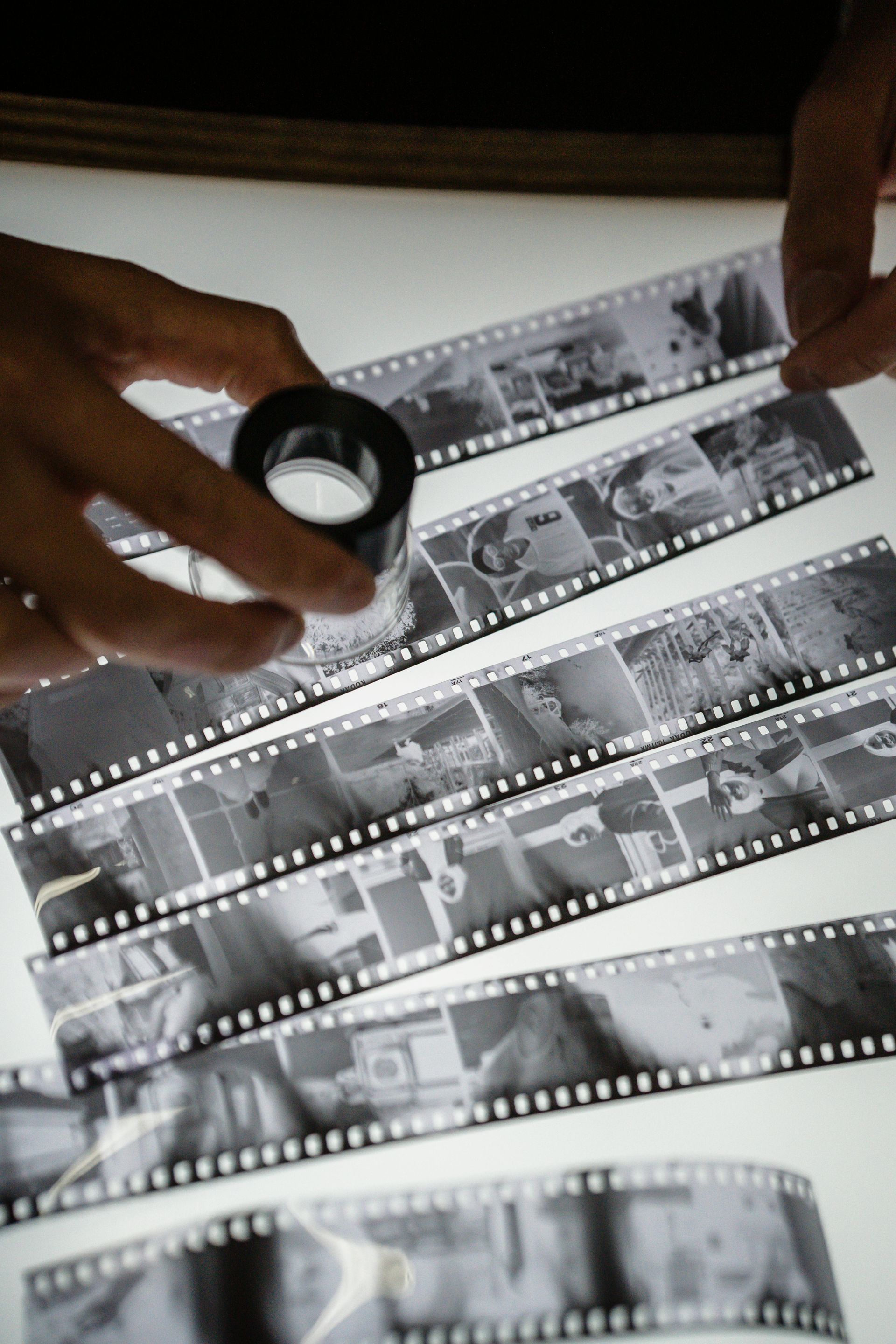 Des mains tenant une loupe au-dessus de bandes de film noir et blanc sur une surface blanche