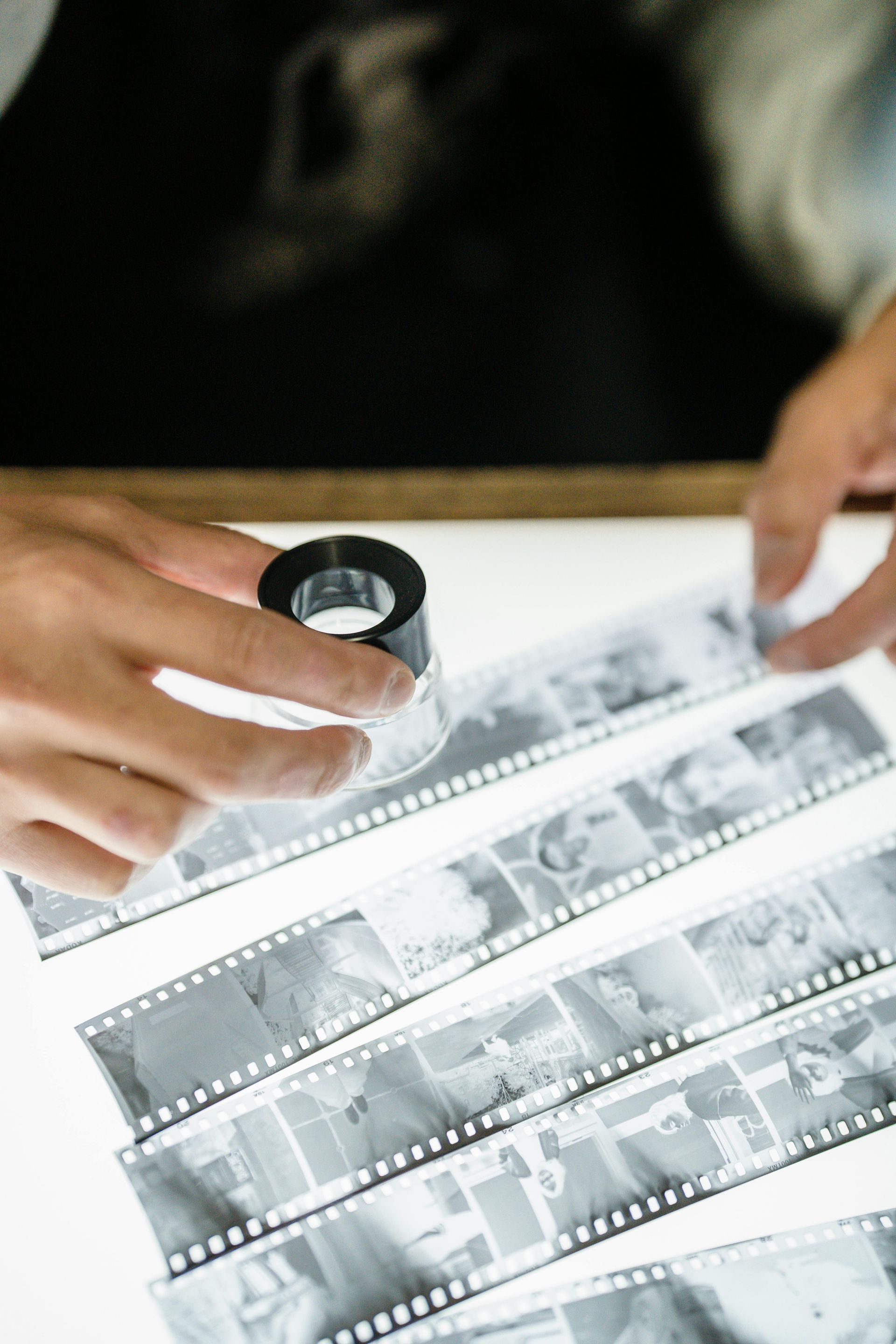 Des mains examinent des négatifs de films à la loupe au-dessus d'une table lumineuse.