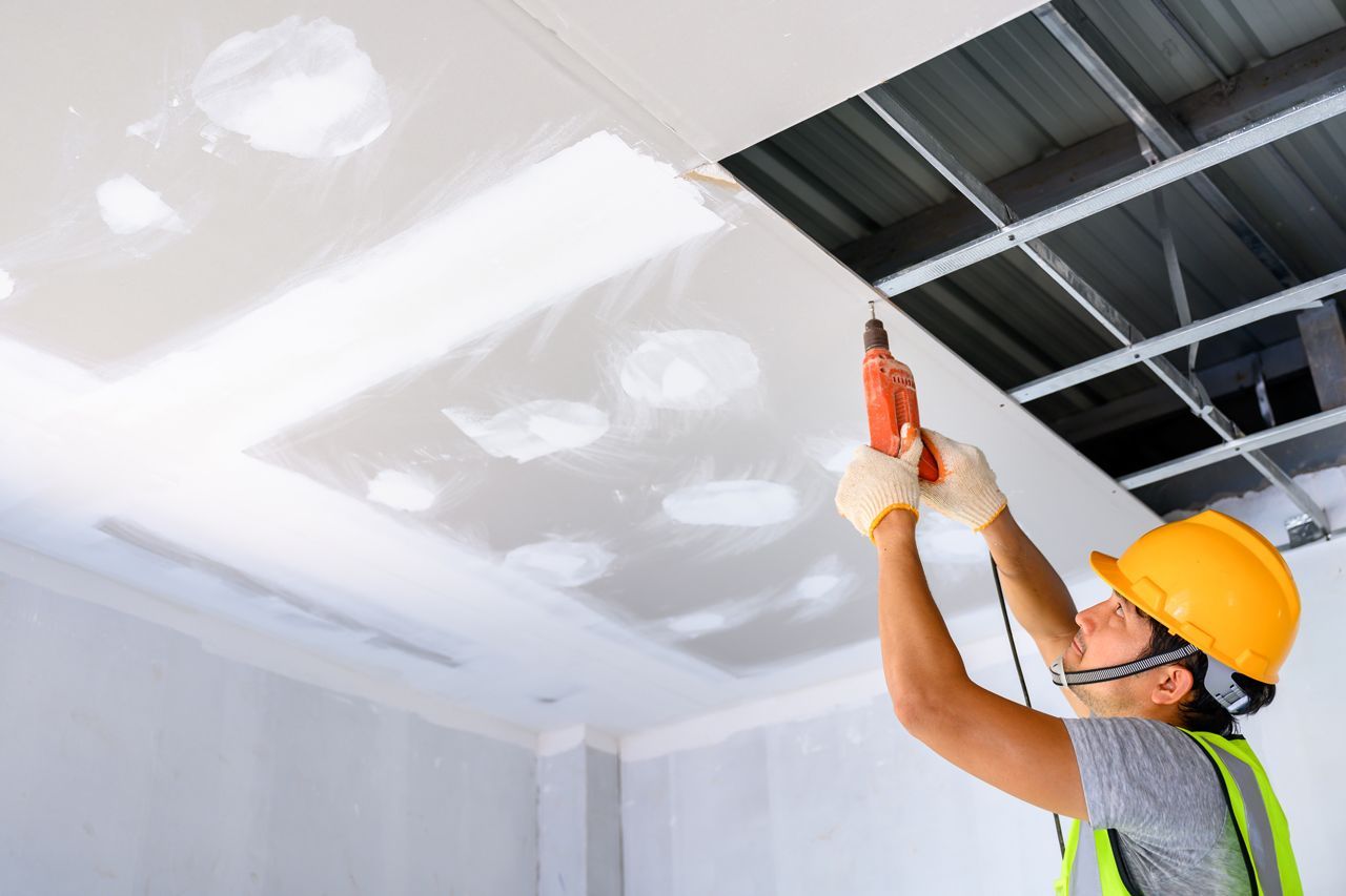 A man is using a drill to fix a ceiling.