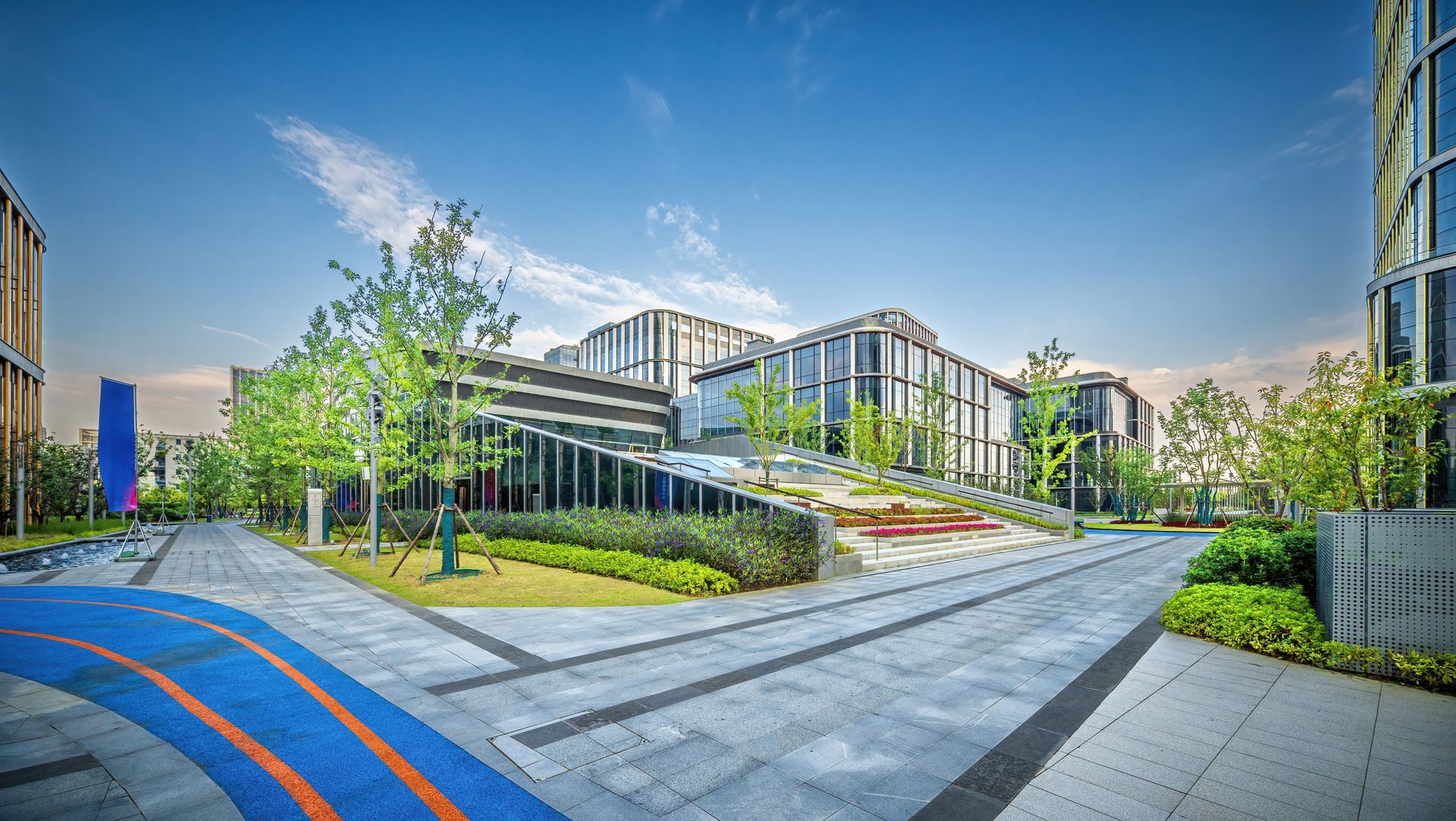 Modern building complex with paved walkways, landscaping, and a blue sky.