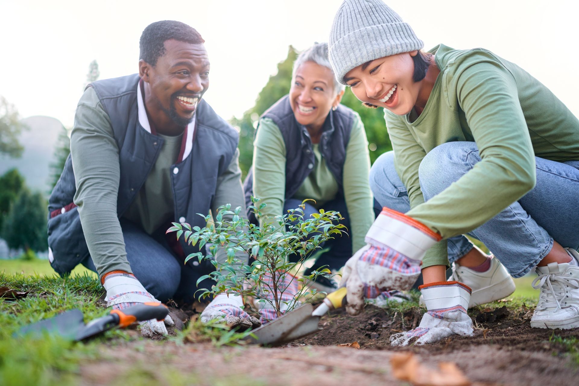 Three people planting a tree, smiling, outdoors.