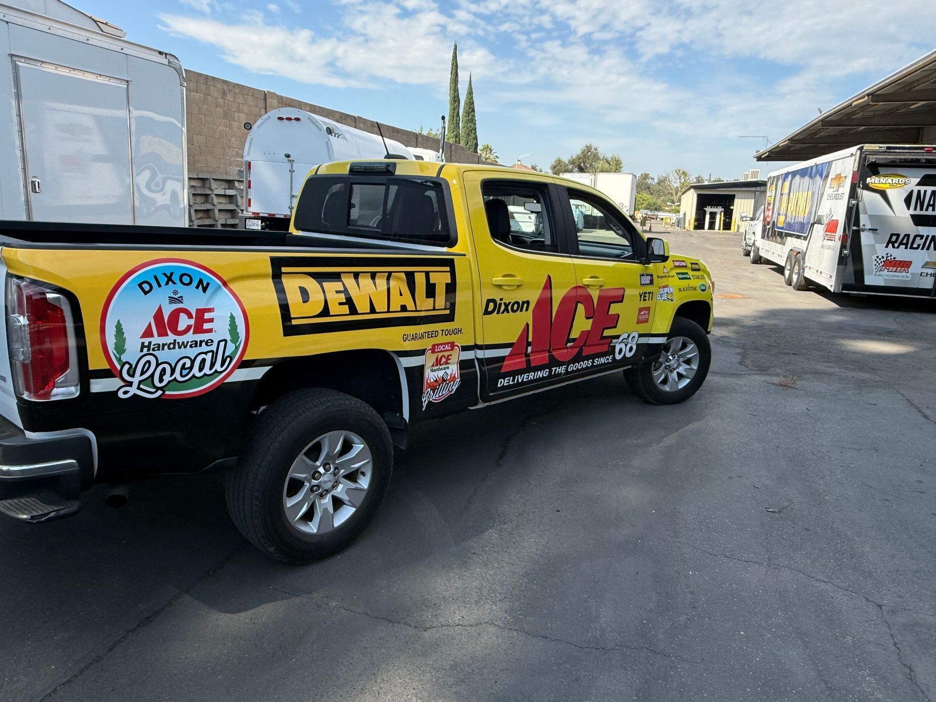 Yellow Ace/DeWalt pickup truck with race decals parked on a street near RVs.