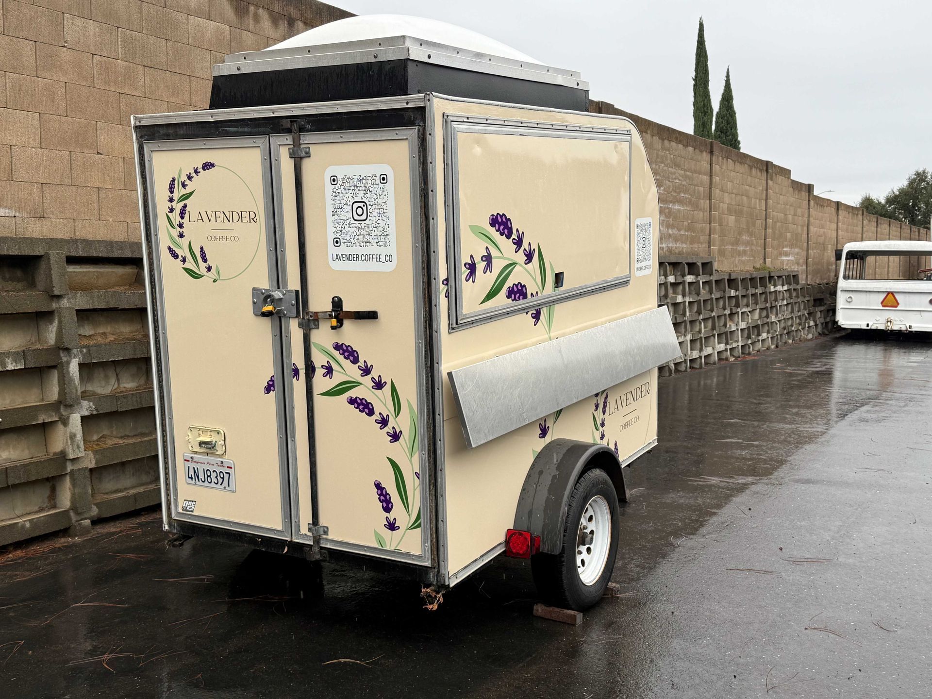 Small cream trailer with floral decals parked on a wet roadside beside a stone wall.