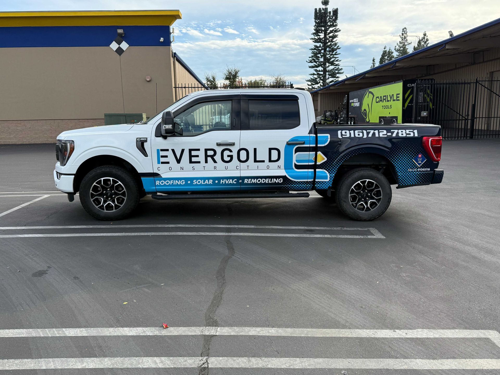 White Evergold pickup truck with blue graphics parked in a lot outside a building