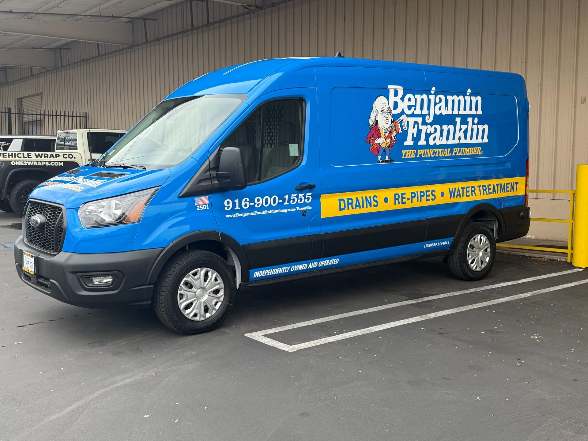 Blue Benjamin Franklin service van parked in a lot, with yellow branding and company contact number on the side