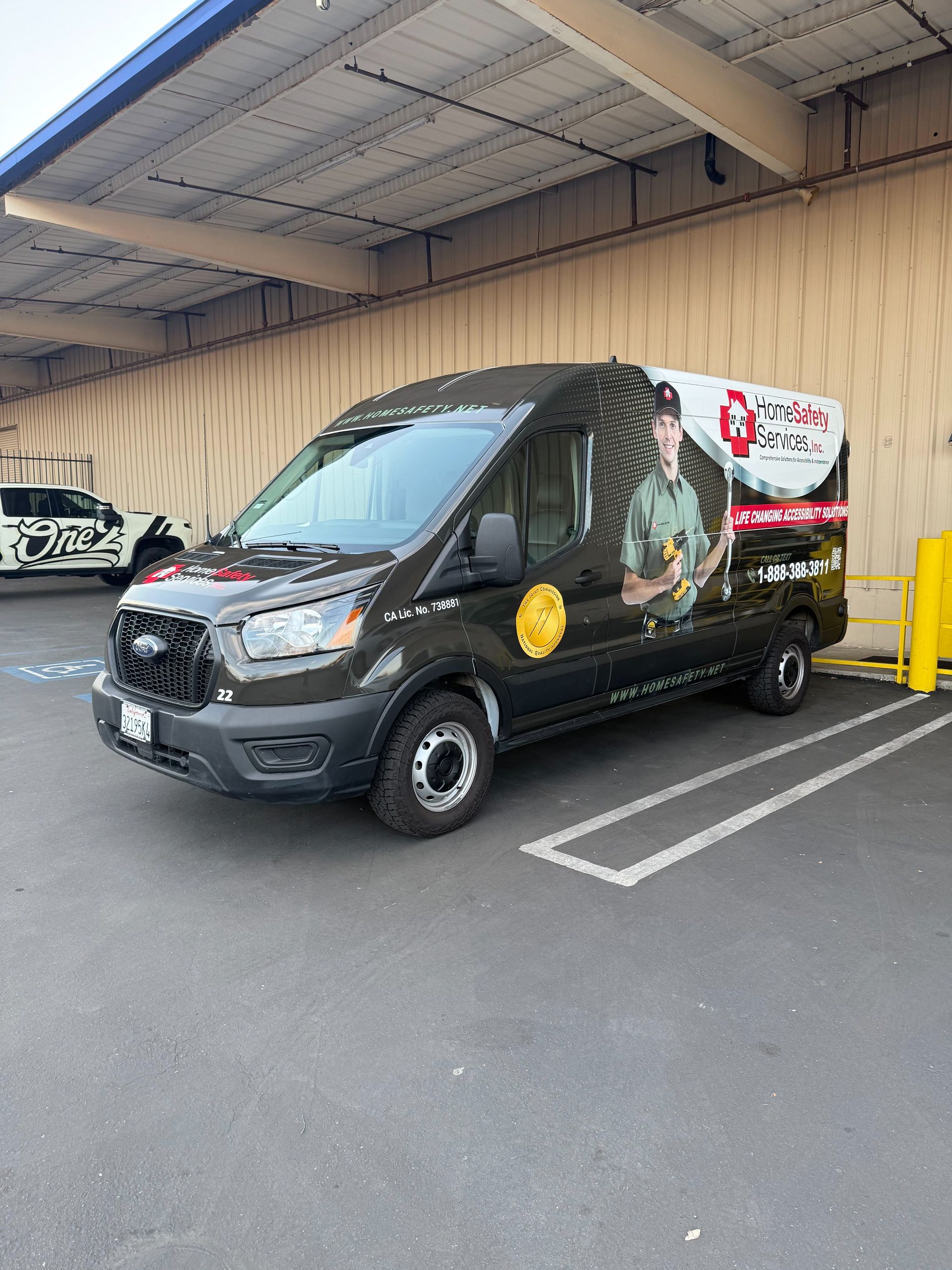 Black van with company logos parked in a covered lot beside yellow bollards and a white car