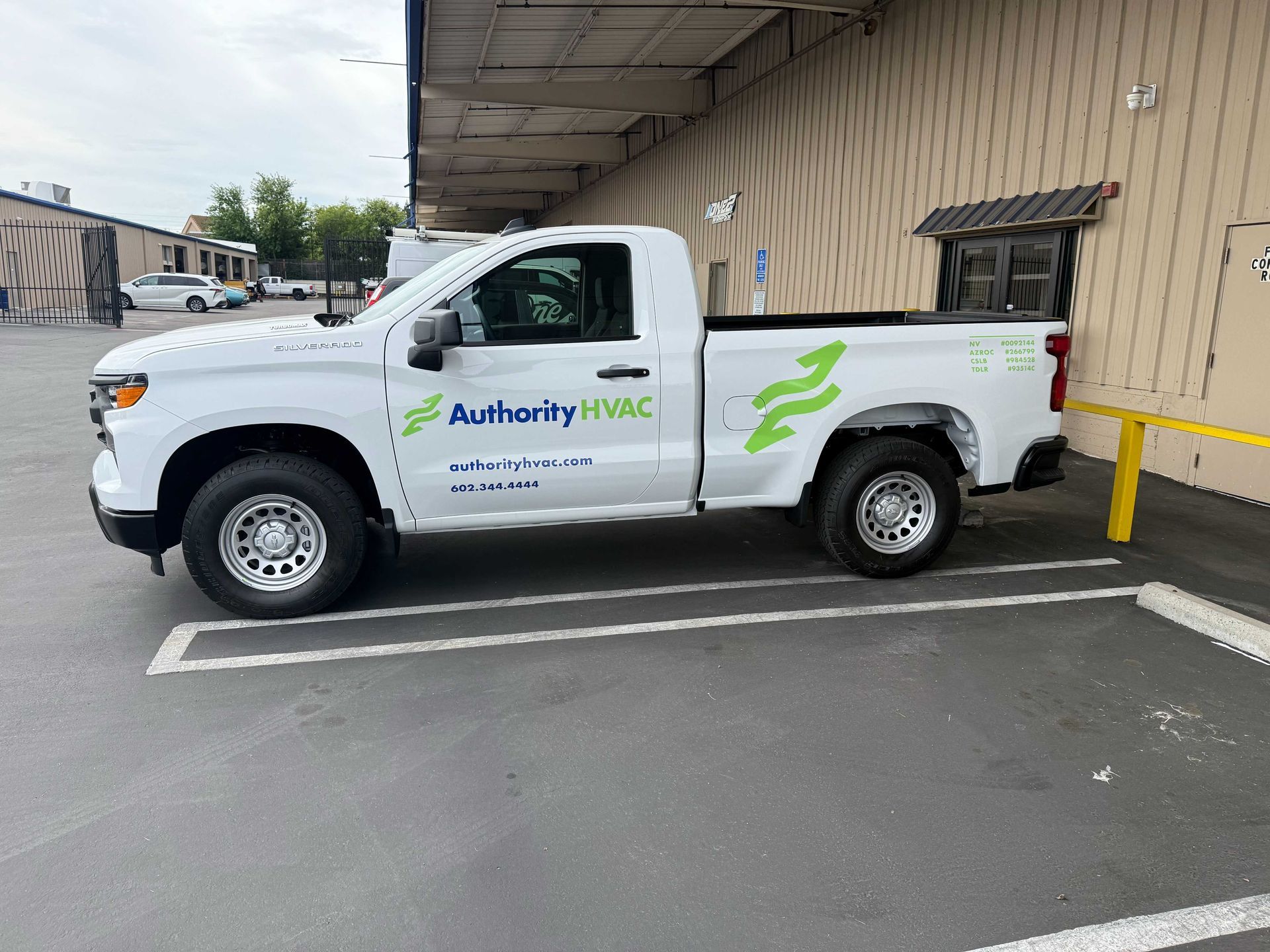 White Authority HVAC pickup truck parked beside a beige building under an awning.