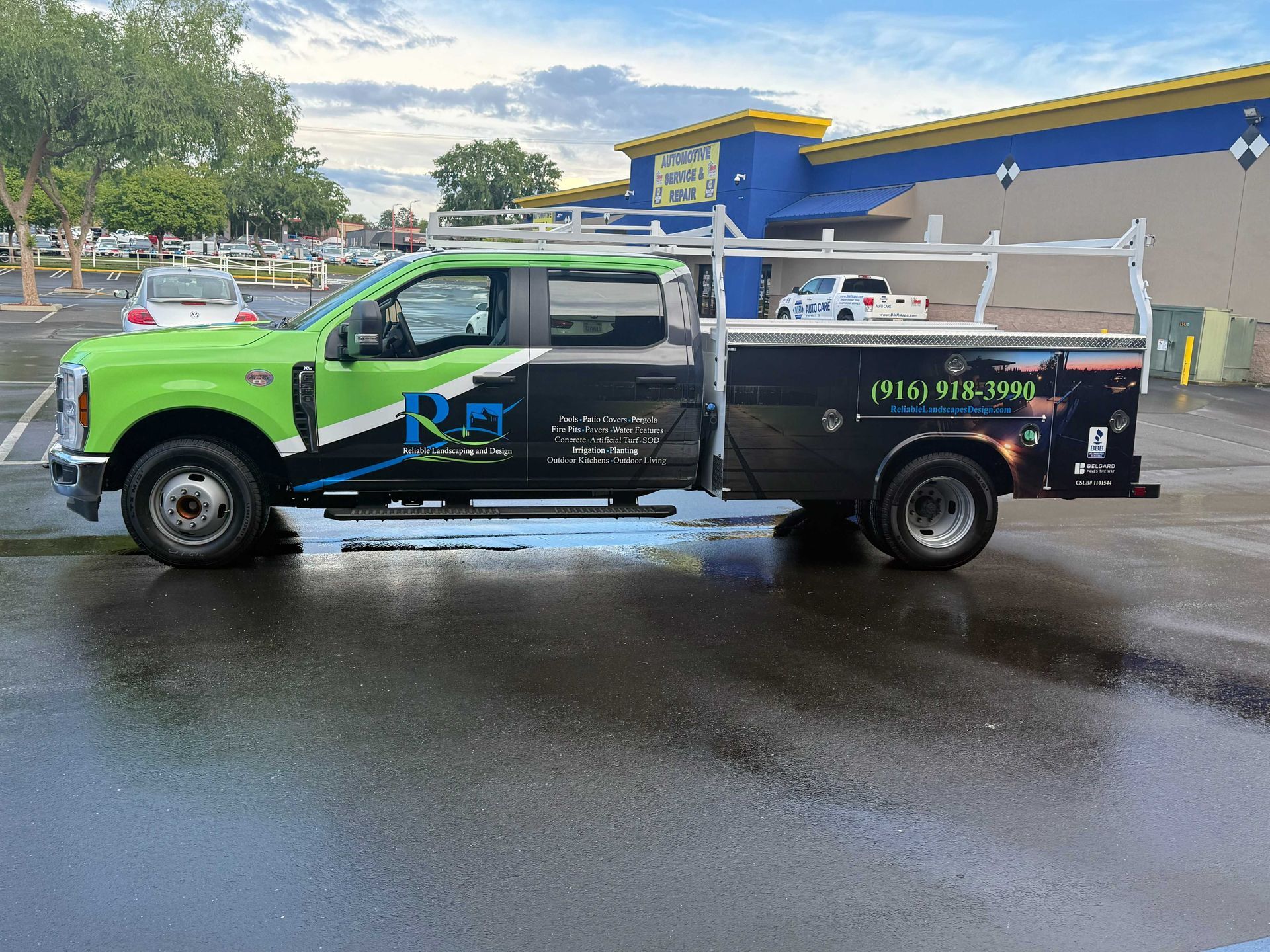 Green and black tow truck parked on a wet street outside a blue building.
