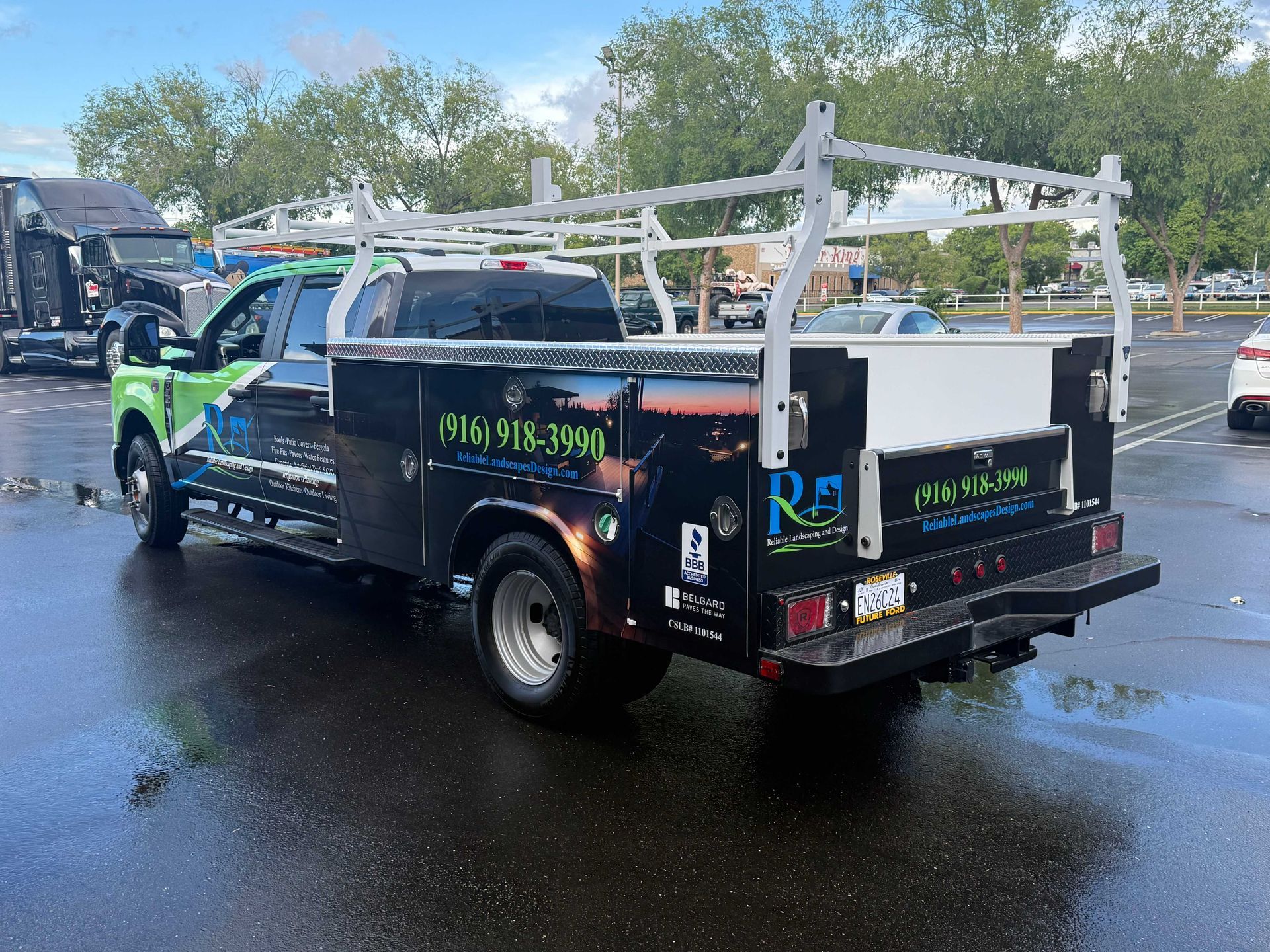 Black utility truck with white ladder racks parked on a wet street outdoors