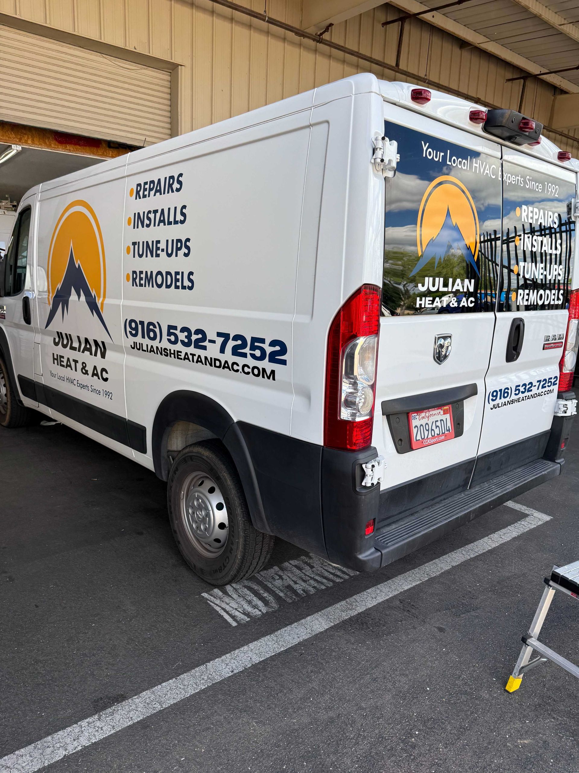 White moving truck parked in a garage, with company branding and contact info on the side and rear.