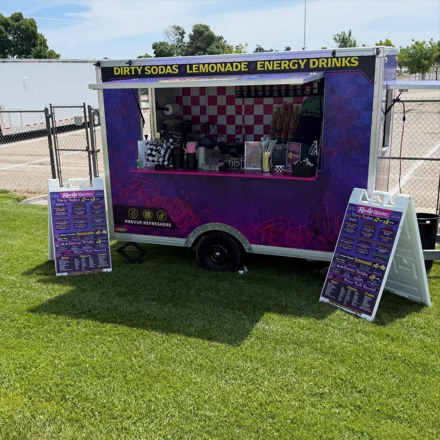 Purple soda-and-lemonade cart with menu boards at an outdoor fair on grass