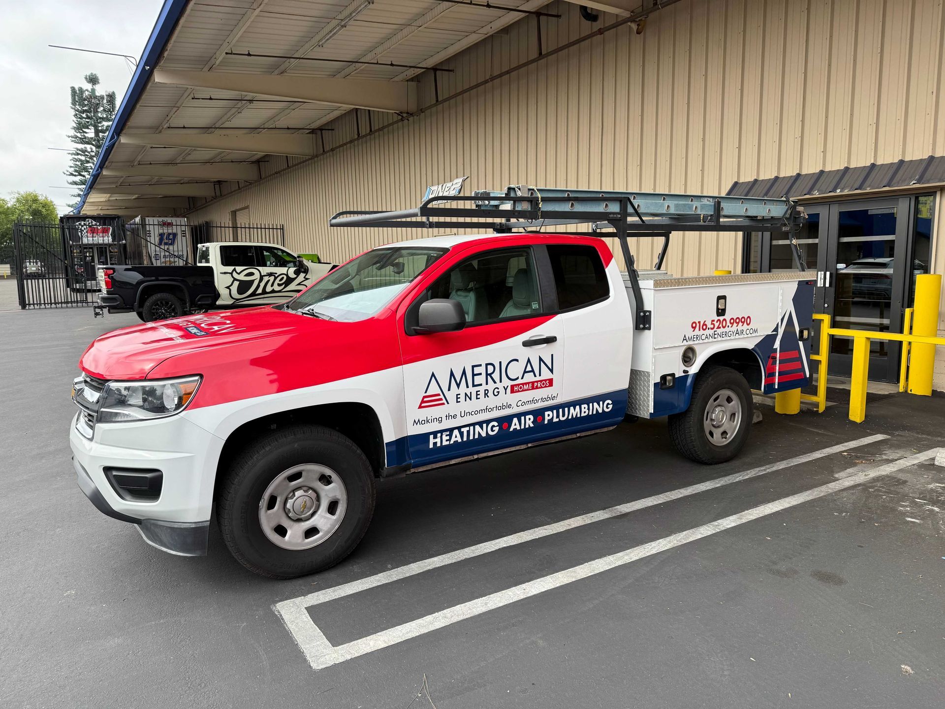 White utility truck with red hood and ladder rack parked by a warehouse loading dock