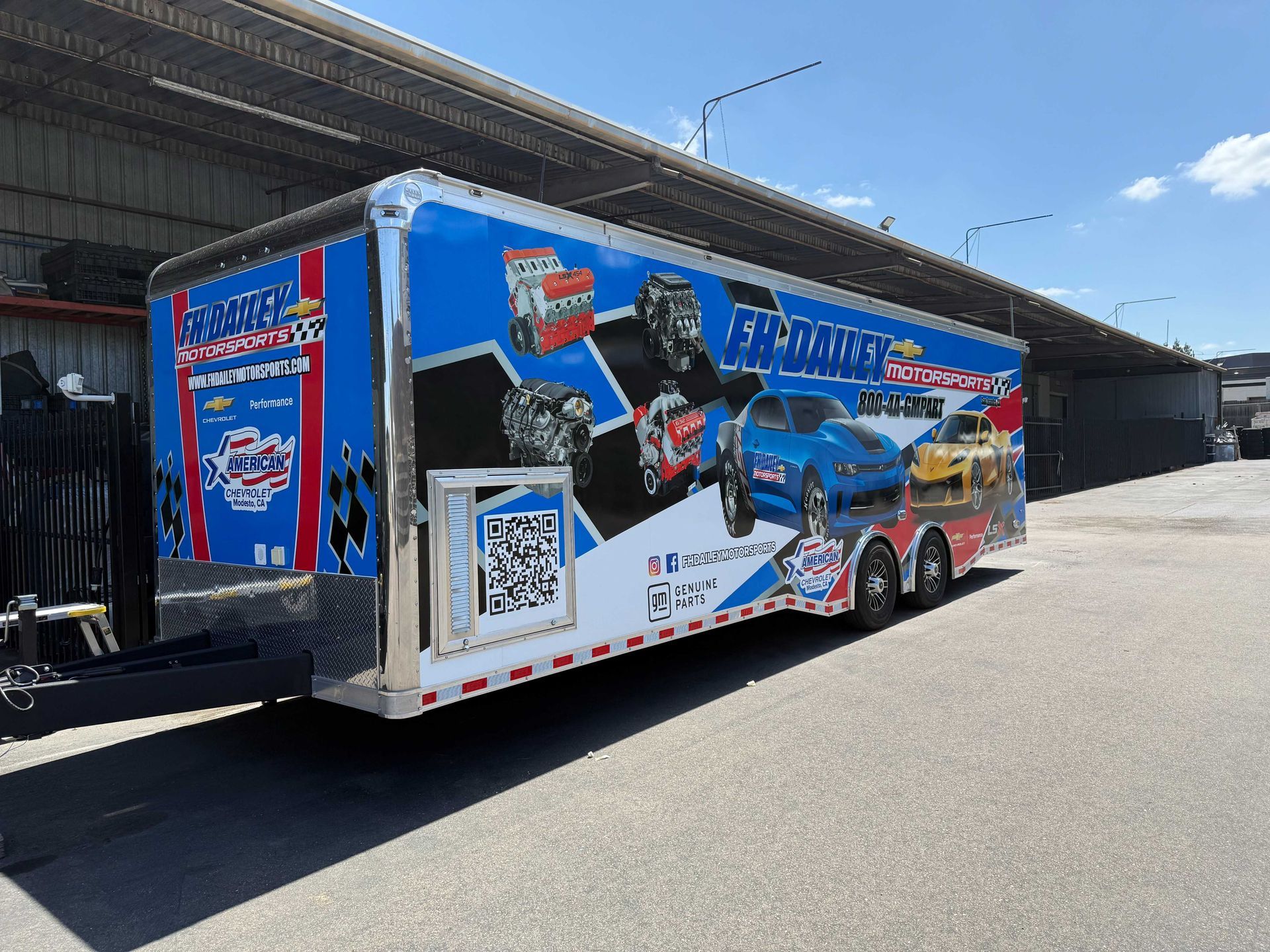 Blue promotional trailer with a large graphic mural parked under an overpass on a sunny day