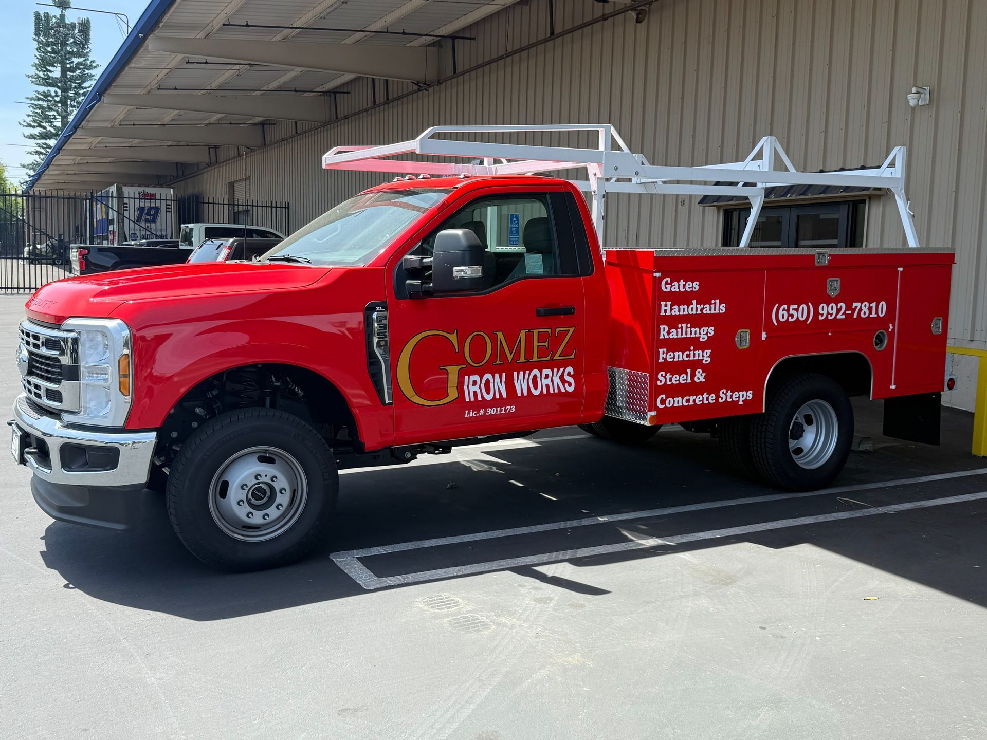Red utility truck with ladder racks parked beside a warehouse loading dock.