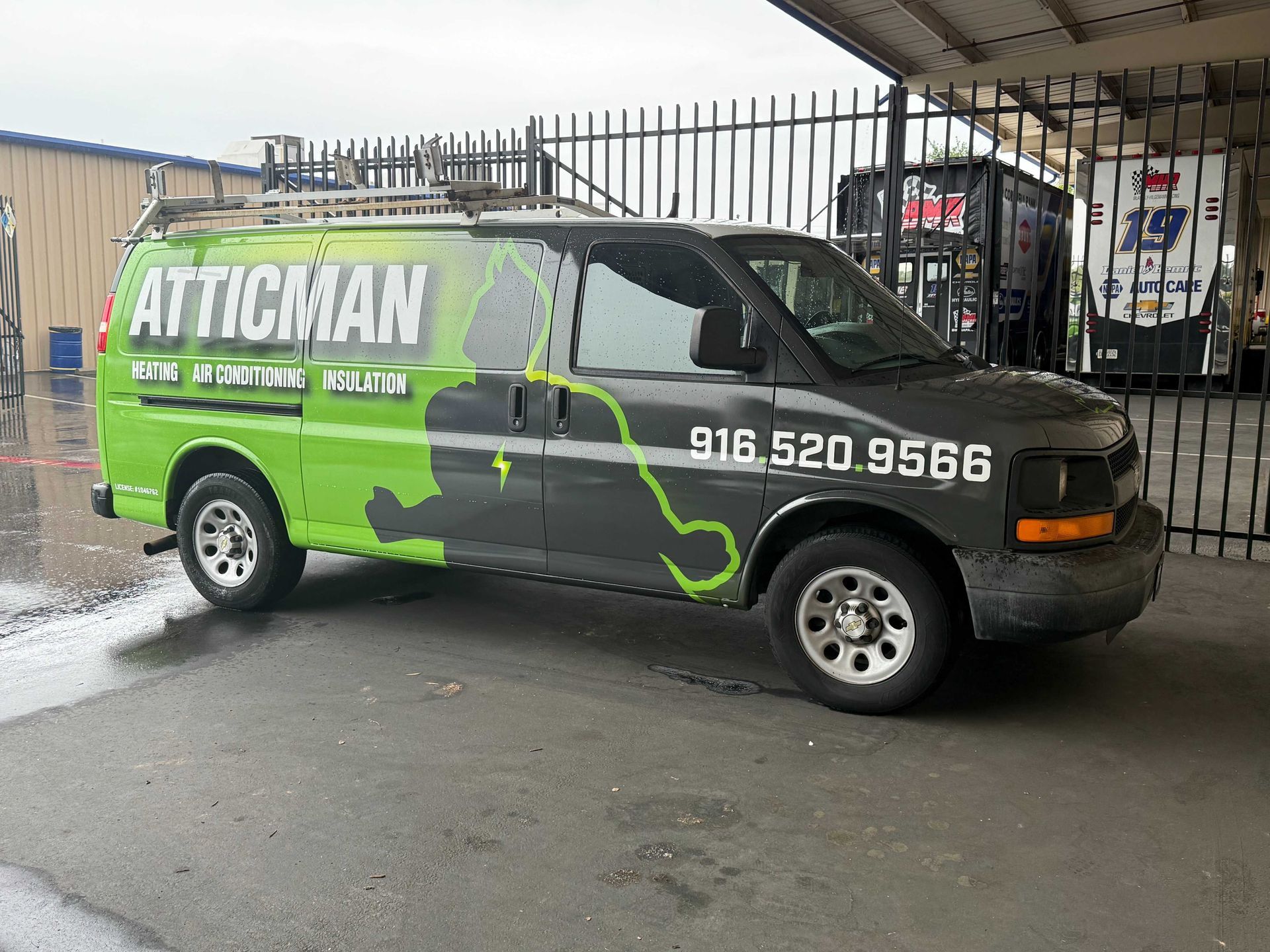 Green Atticman service van parked by a fence on a wet street, with phone number on the side.