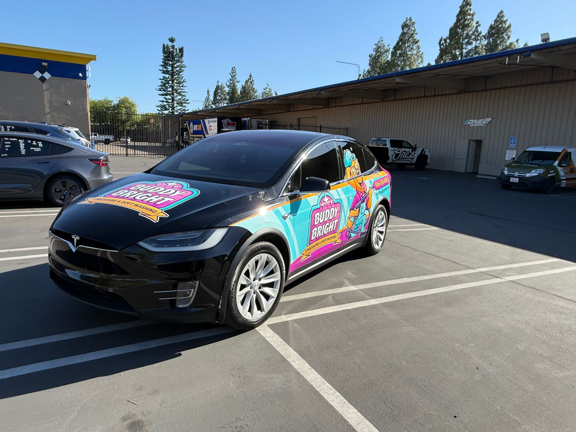 Black SUV with colorful graphics parked in a sunlit lot beside a building