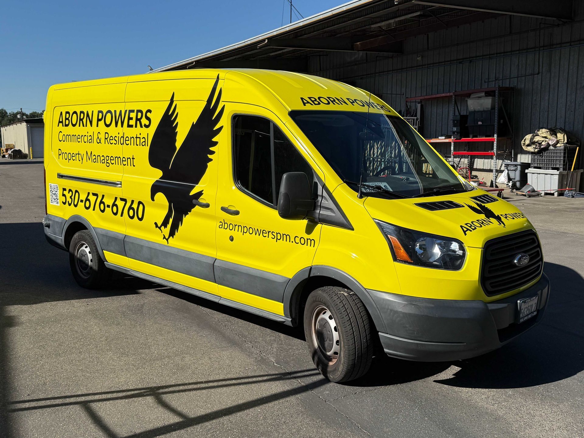 Yellow delivery van with black bird graphic parked outdoors on a sunny street