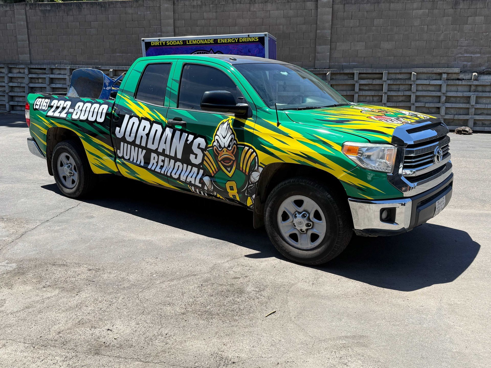 Green Jordan’s junk removal pickup truck parked outdoors in sunlight, with bold yellow and white graphics.