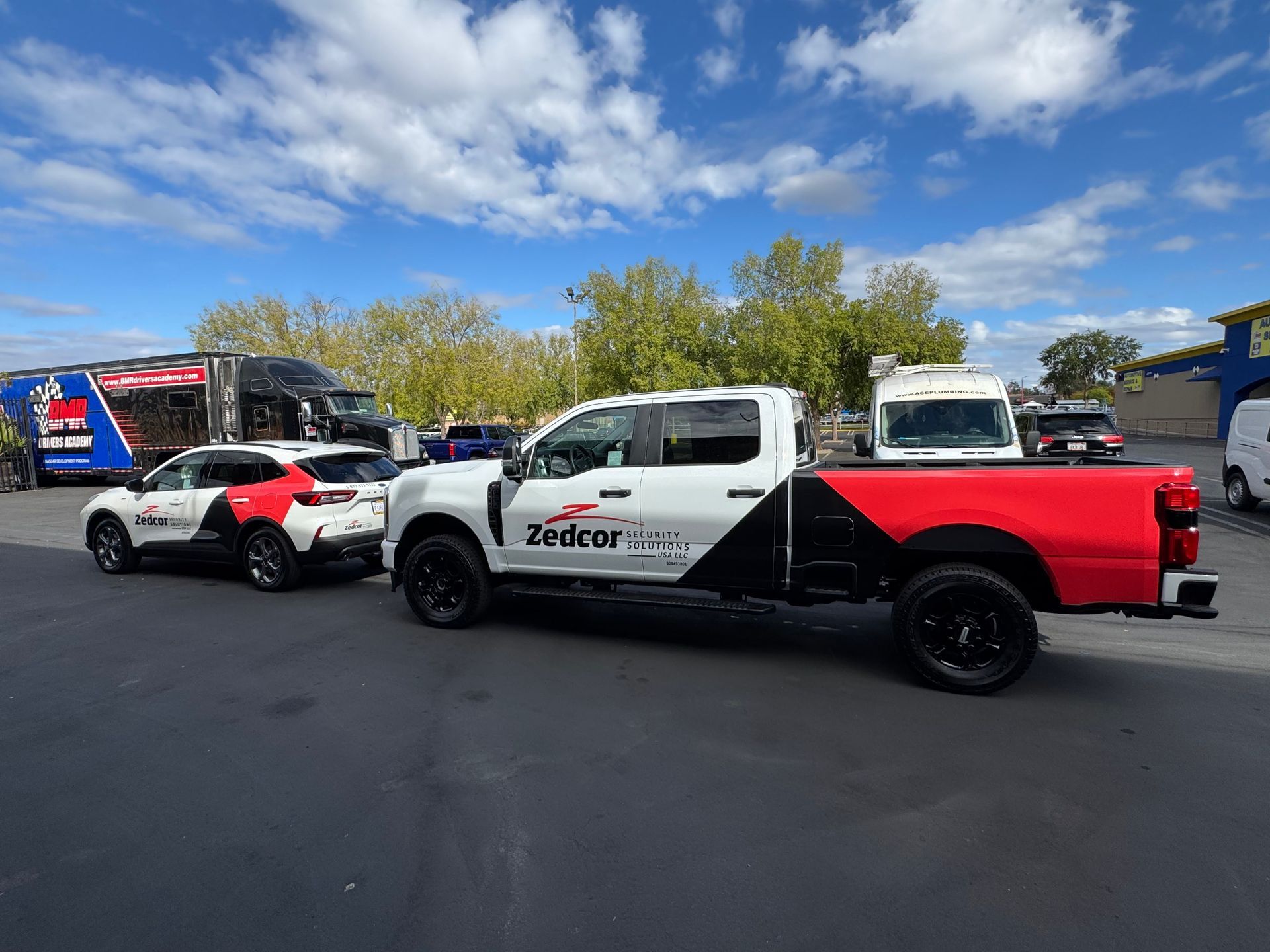 Red, white, and black lifted pickup trucks parked in a lot under a blue sky