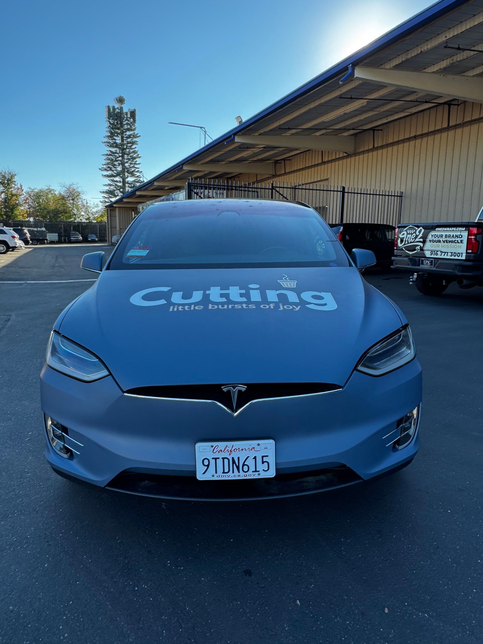 Blue car with “Cuttis” on the hood parked under an awning in a lot