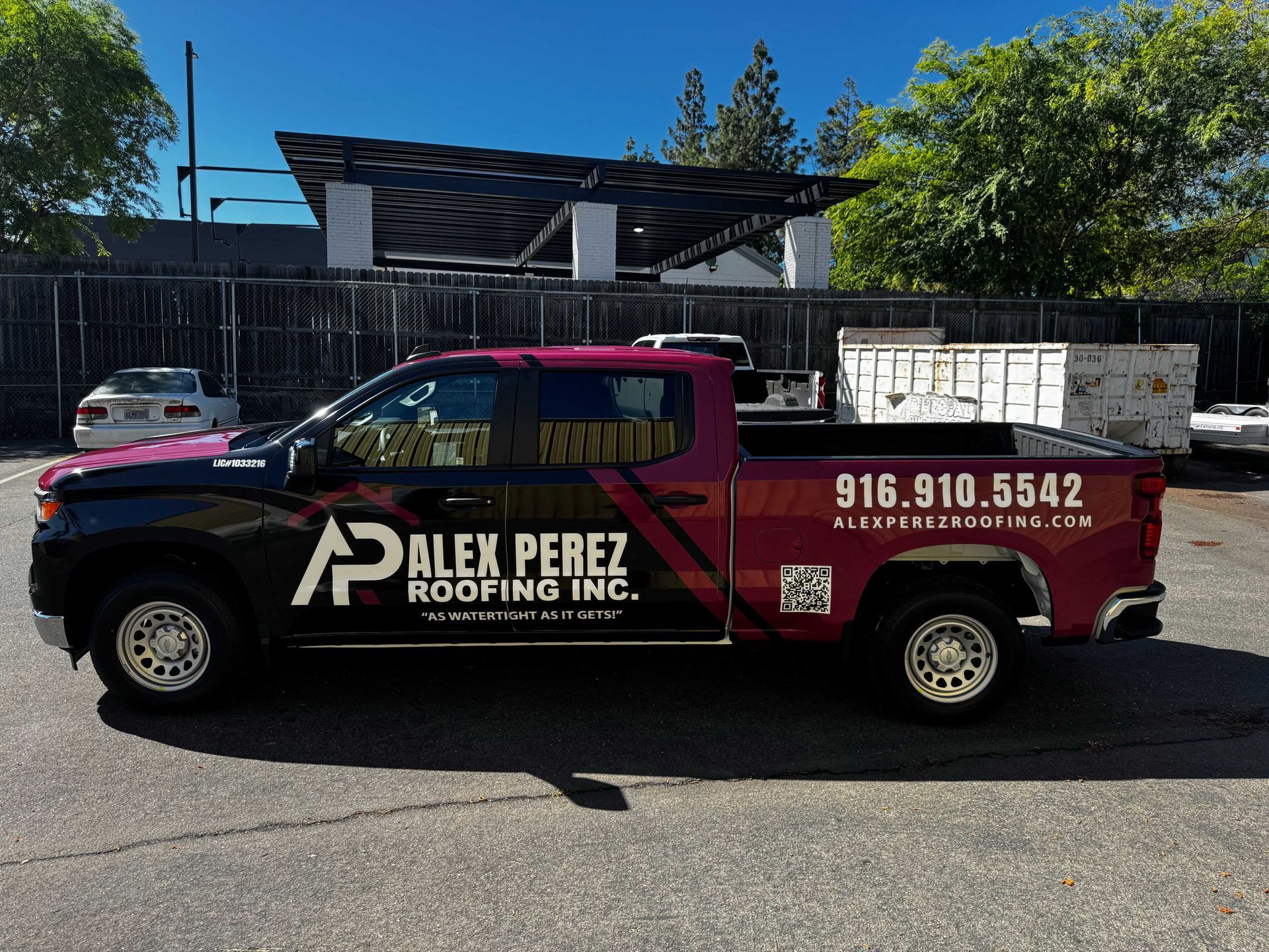 Red and black Alex Perez Roofing Inc. pickup truck parked on a street in front of a building.