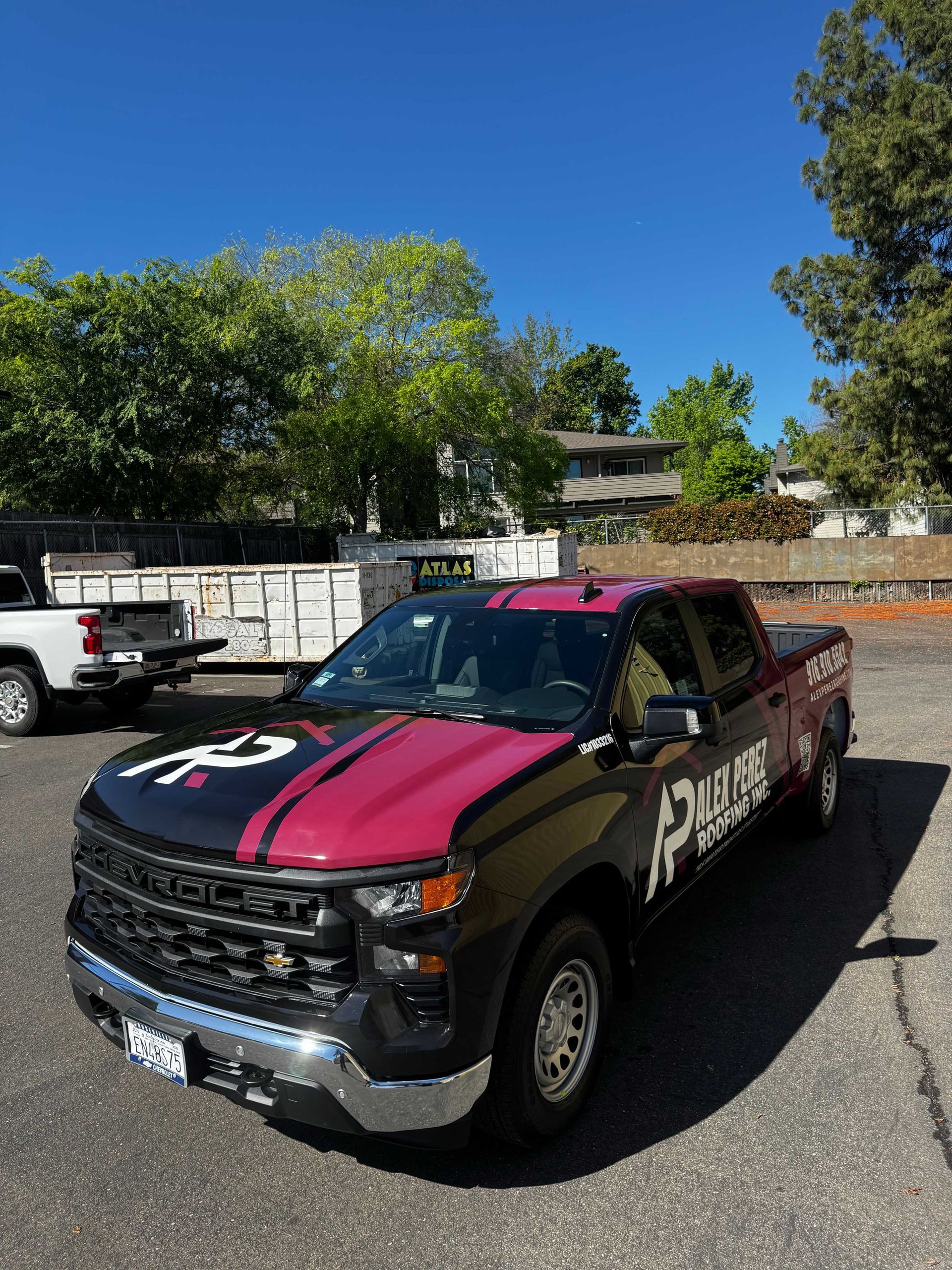 Black-and-pink custom pickup truck parked on a sunny street, with palm trees and other vehicles nearby