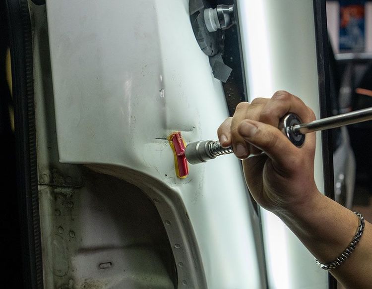 Hand sanding a white car panel with a red sanding block and a tool in the other hand